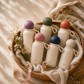 Six cream Haven & Elm Pebble insulated kids water bottles with round colored lids in a wicker basket