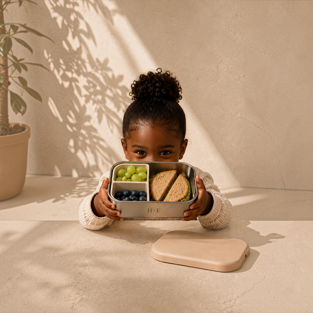 Child holding an open Fen lunch box with sandwich, grapes and blueberries